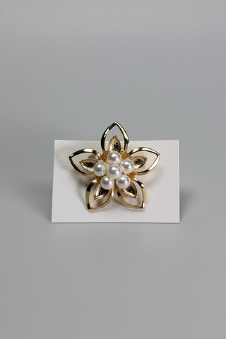 A gold flower brooch with white faux-pearl accents, displayed on a small white card over a textured white fabric background.