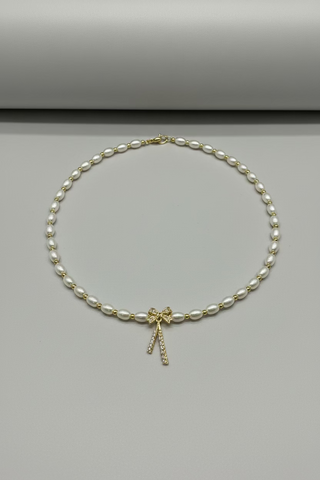 A pearl and gold beaded necklace with a bow-shaped gold pendant, displayed on a textured white towel.