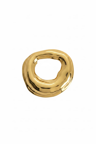 A chunky, organic-shaped gold brooch with a highly polished, reflective finish, displayed on a small white backing card against a textured white background.