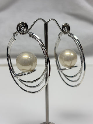 A pair of silver-toned double-hoop earrings with a central cream-colored pearl, displayed on a metal stand against a light gray background.