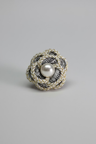 A decorative fabric flower-shaped brooch with braided black and white tweed petals, a gold braided edge, and a central white pearl