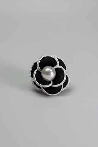 A black and silver flower-shaped brooch with a central white pear