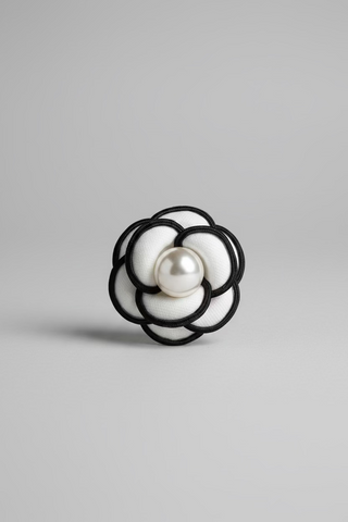 A black and white flower-shaped brooch with a white pearl at the center