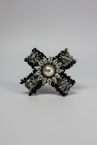 A black tweed bow brooch with a central white faux pearl and clear rhinestone accents