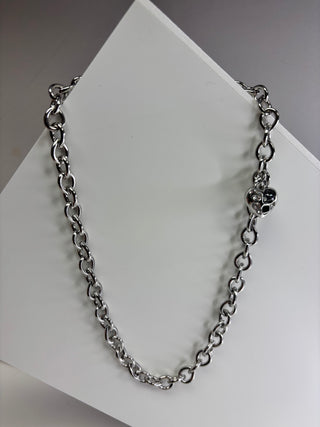 A silver-toned metal chain necklace with heart-shaped links and a small heart charm, displayed on a white geometric surface.