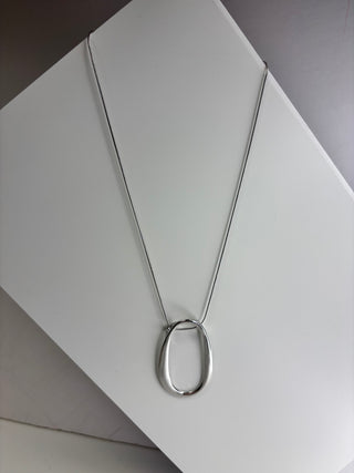 A silver-toned necklace with a minimalist, open oval pendant on a fine chain, displayed on a white geometric surface.