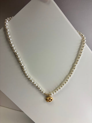 A single-strand white pearl necklace with a small gold pendant, displayed on a white jewelry stand.