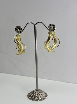 A pair of gold-toned textured spiral drop earrings displayed on a silver-tone jewelry stand against a plain light gray background.