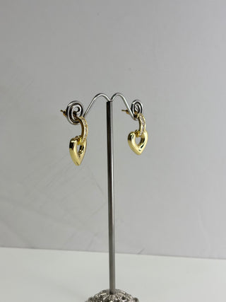 A pair of gold heart-shaped dangle earrings displayed on a silver wire jewelry stand against a plain light gray background.