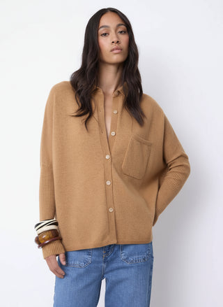 Woman wearing a beige button-up shirt and blue jeans against a white background