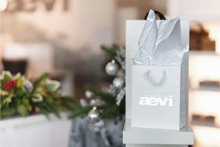 Silver gift bag with 'aevi' branding on a blurred festive background
