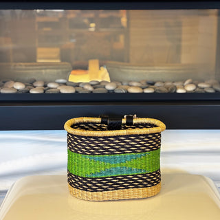 Woven basket with black, blue, and green stripes on a surface in front of a fireplace.