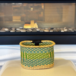 Woven basket with green and blue pattern on a white surface with a blurred background
