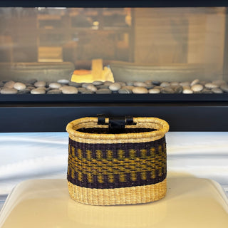 Woven basket with black and gold pattern on a white surface in front of a fireplace.