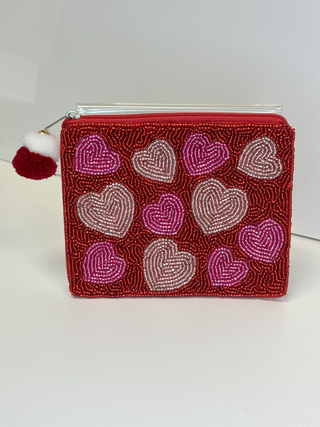 A red coin purse with a pattern of pink and white hearts, featuring a zipper closure and a small tassel.